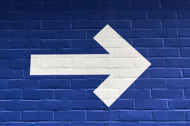 A white arrow on a blue-painted brick wall.